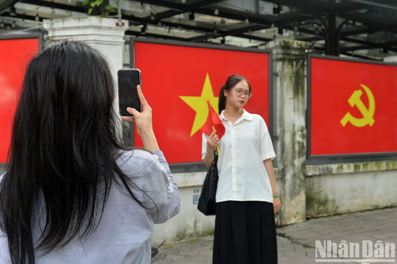 A girl takes a photo of her friend against a background of the Party flag and national flag. A girl takes a photo of her friend against a background of the Party flag and national flag.