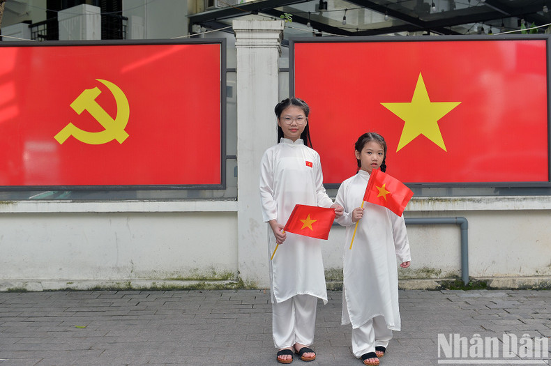 Two little girls pose for a photo with the Party flag and national flag in the background. Two little girls pose for a photo with the Party flag and national flag in the background.