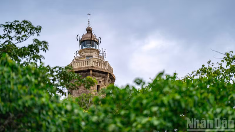 The lighthouse’s distinctive octagonal tower rises above the landscape, its solid silhouette set against the deep blue sky — a steadfast symbol amid wind and wave.