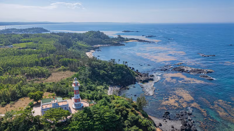 At low tide, the waters surrounding the rocky cape reveal an ancient volcanic crater alongside vibrant carpets of seaweed and coral, transforming the area into a living “lava museum”.