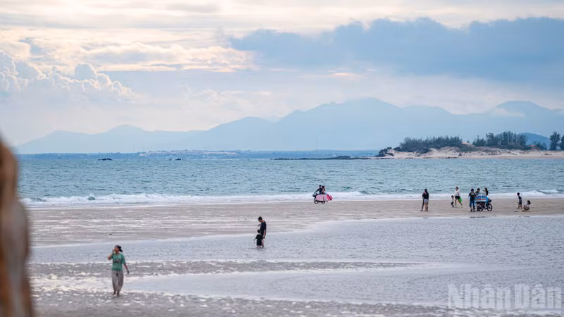 Streams of visitors make their way across the exposed seabed, with gentle waves lapping against the wet sand on either side.