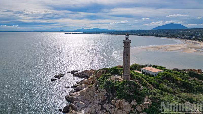 The lighthouse’s distinctive octagonal tower rises above the landscape, its solid silhouette set against the deep blue sky — a steadfast symbol amid wind and wave.