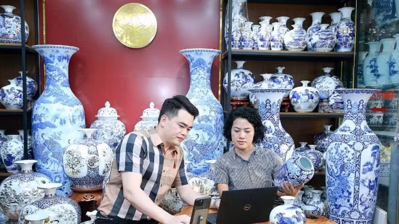 Artisan Tran Trung Hieu (Bat Trang Commune, Gia Lam District, Ha Noi) shares with a fellow artisan the process of listing products on e-commerce platforms. (Photo: HUY HOANG)