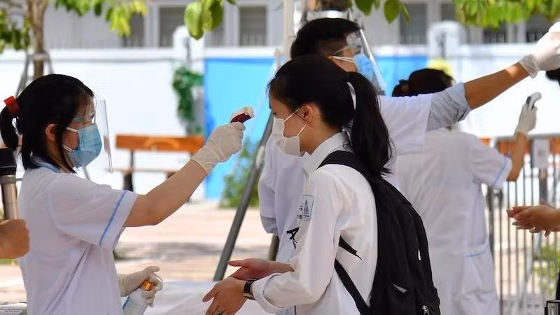 A student has her body temperature checked before entering the exam room.